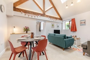 A modern living room with a teal sofa, a dining area with red chairs, and a kitchen area with a wooden ceiling. - 2 Bed in Uttoxeter (oc-q33072) (Prestwood)