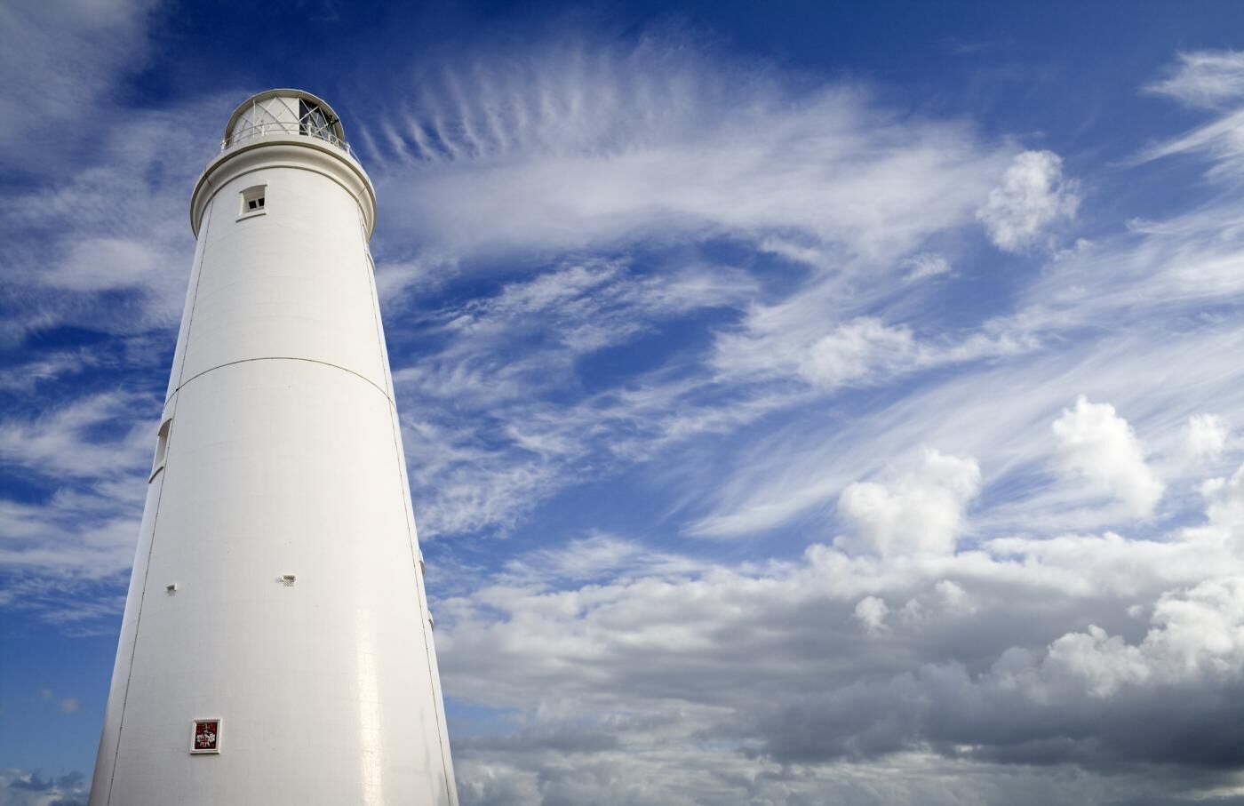 A tall, white lighthouse against a partly cloudy sky.