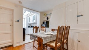 Un coin repas avec une table dressée pour quatre personnes, des chaises en bois, une cuisine en arrière-plan et une porte blanche.