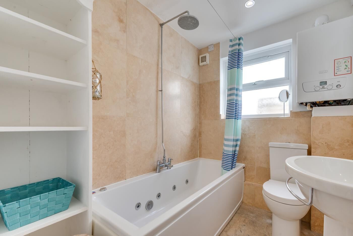 Een badkamer met bad, toilet en wastafel, met beige tegels en een raam.