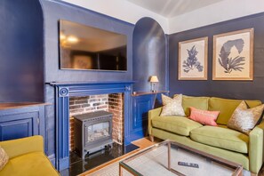 A living room with a fireplace, a sofa, and framed artwork on the wall. - 4 Bed in Southwold (oc-park) (Southwold)