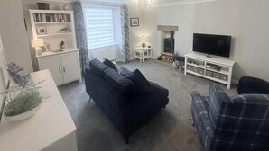 Una sala de estar con un sofá, una televisión, una chimenea, una estantería y una mesita de noche con una lámpara.