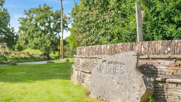 A stone wall with the word "ASHES" carved into it, surrounded by a grassy area and trees. - 4 Bed in Hawes (oc-g33122) (Hawes)