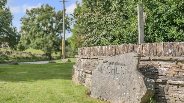 Eine steinerne Mauer mit der Inschrift 'ASHES' auf einer grünen Fläche.