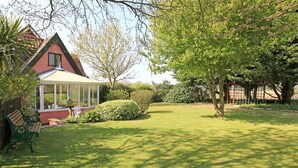 A house with a conservatory, a well-maintained lawn, and a large tree. - 1 Bed in Frostenden (oc-phc) (Frostenden)