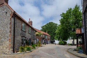 A street with stone buildings, a paved road, and greenery. - 2 Bed in Holt (oc-1267) (Holt)