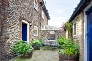 A stone building with a blue door, a small table with chairs, and potted plants. - 2 Bed in Holt (oc-1267) (Holt)