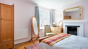 Quarto com cama, cômoda, cadeira, espelho e lareira.