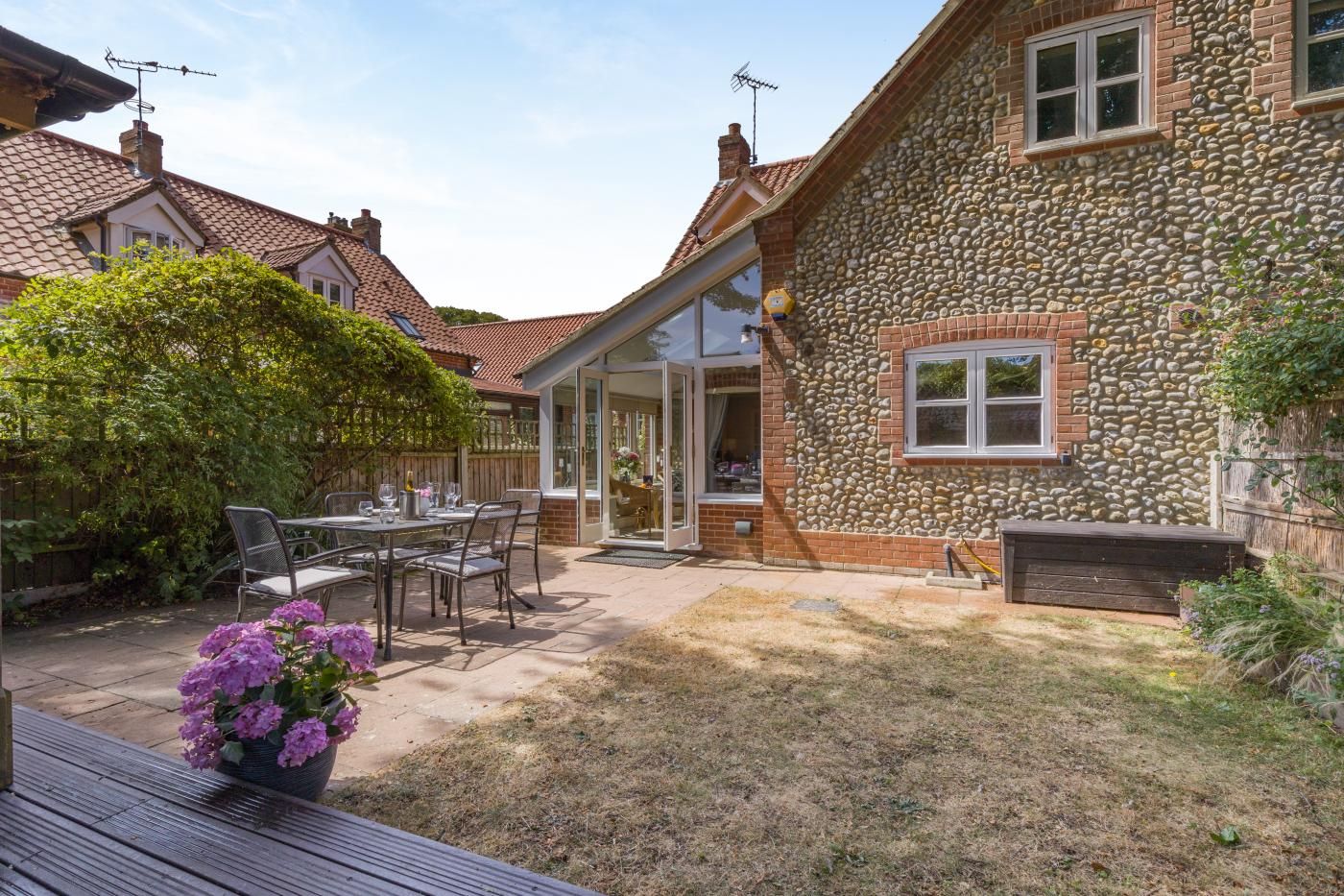 A house with a stone exterior, a patio with a table and chairs, and a garden with purple flowers.