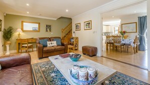 A living room with a brown leather sofa, a coffee table with decorative items, a staircase, and a dining area with wooden furniture. - 2 Bed in Blakeney (oc-1558) (Blakeney)