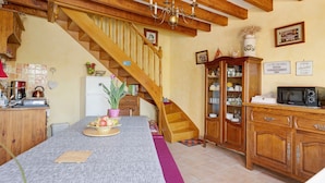 Une cuisine avec un escalier en bois, une table à manger ornée d’un vase et un four à micro-ondes posé sur un meuble en bois.