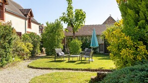 Un jardin bien entretenu, avec une pelouse, une pergola surmontée d’un parasol bleu et des meubles pour s’asseoir à l’extérieur.
