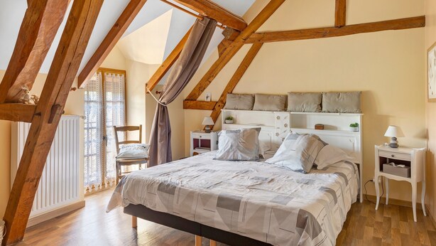 Une chambre avec un plafond en pente, un lit recouvert d’une couvre-lit à motifs, une table de chevet avec une lampe et une chaise.