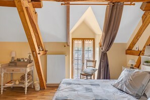 A bedroom with a sloped ceiling, a wooden bed frame, a bedside table, a chair, and a window with curtains. - Guest Room 'Chambre Automne' with Shared Garden and Wi-Fi (Villefranche-sur-Cher)