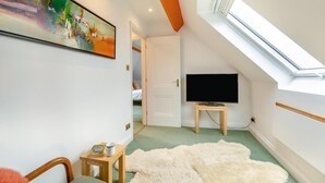A room with a skylight, a television on a stand, a painting on the wall, and a door leading to another room. - 1 Bed in Clatcombe (oc-s33309) (Castleton)