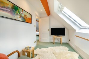 A room with a skylight, a television on a stand, a painting on the wall, and a door leading to another room. - 1 Bed in Clatcombe (oc-s33309) (Castleton)