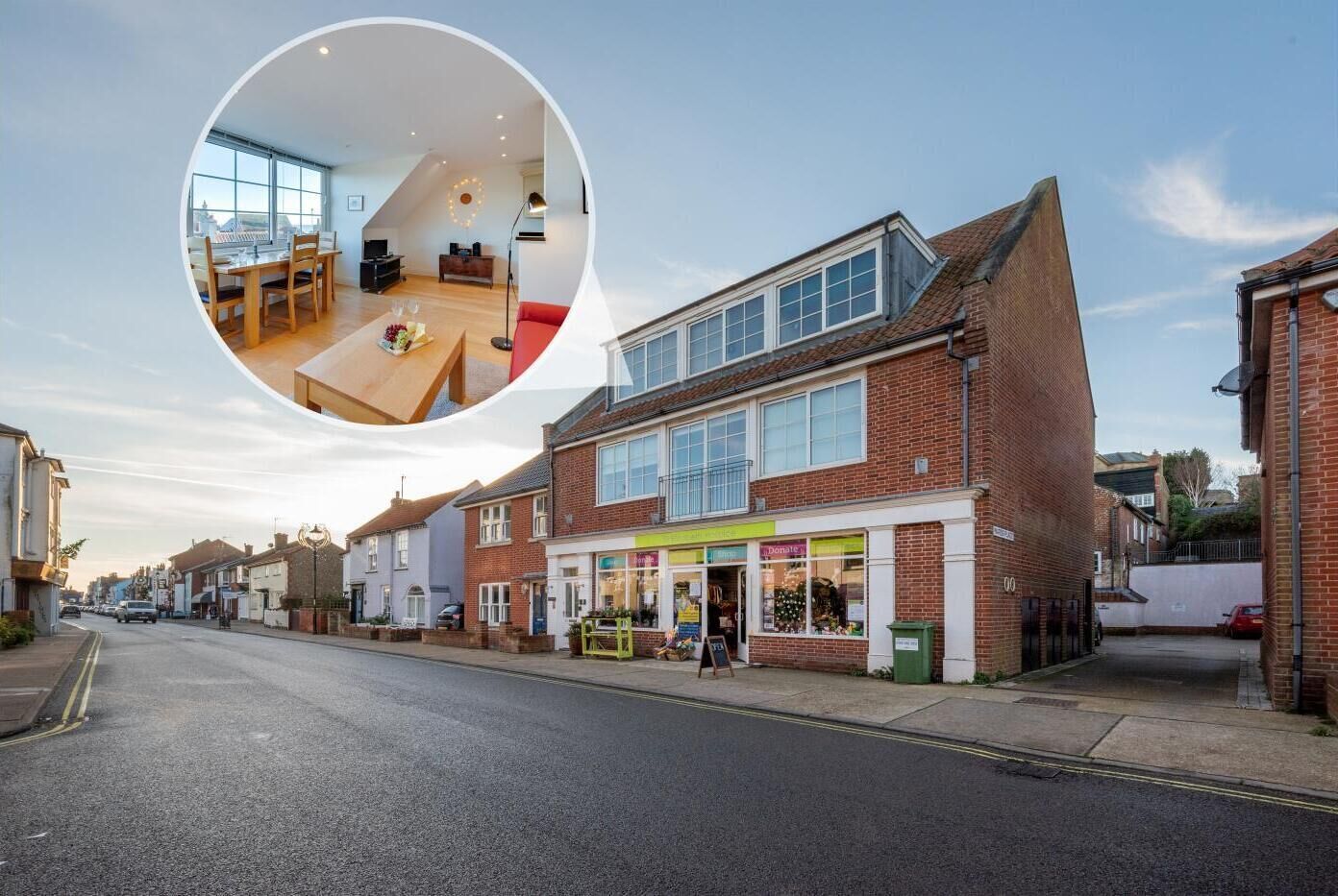 A street view of a town with a two-story building featuring a shop on the ground floor and a residential unit above.