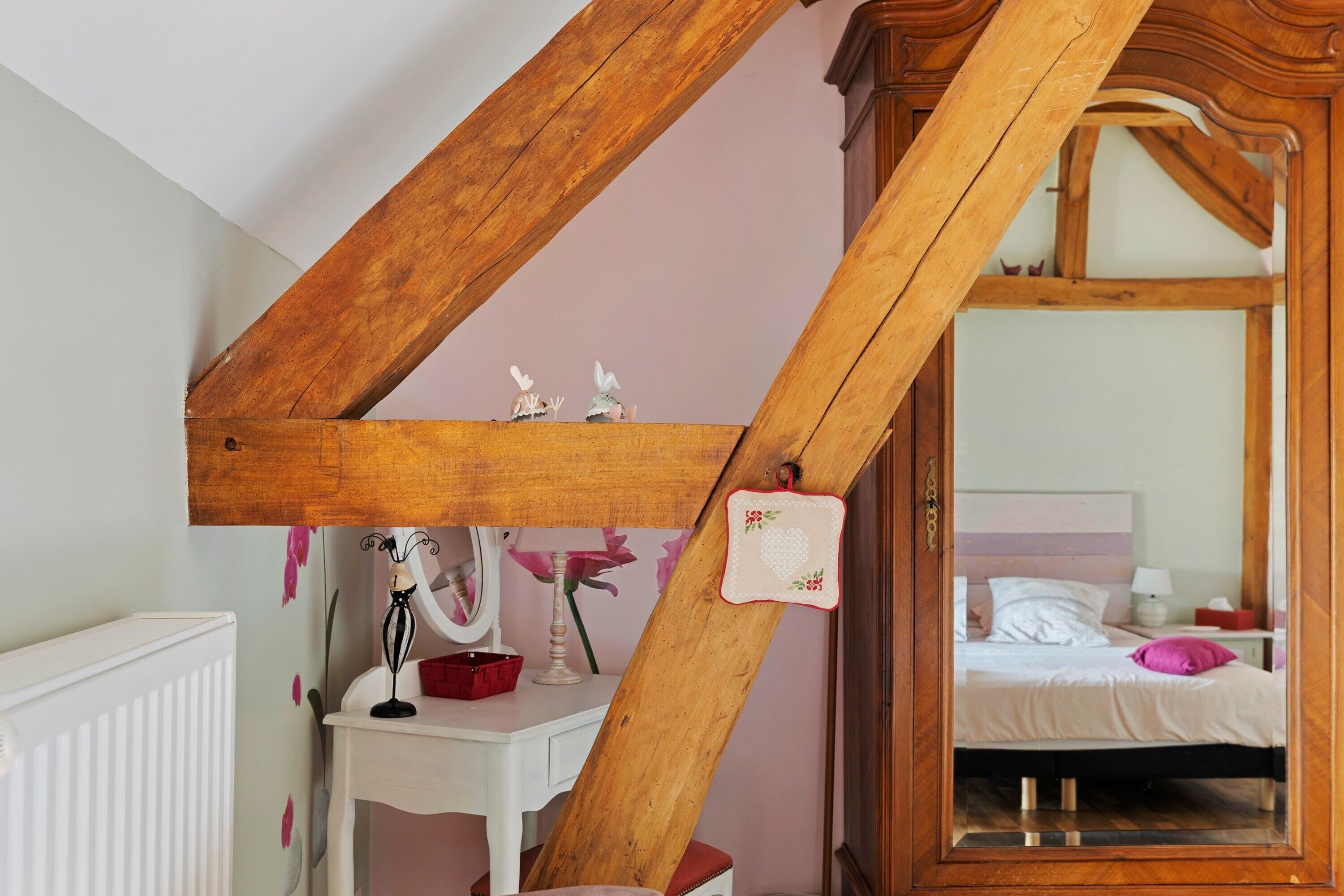 Un dormitorio con techo inclinado, cabecera de madera, mesita de noche, espejo y cama con almohadas.