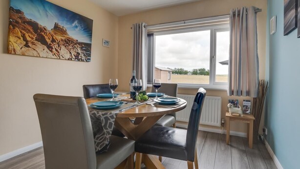 Ein Essbereich mit einem runden Tisch, Stühlen und Blick auf die Landschaft durch ein Fenster.