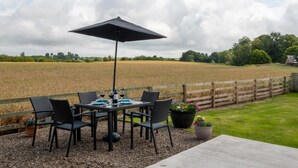 Eine Terrasse im Freien mit Tisch, Stühlen, einem schwarzen Sonnenschirm und Blumentöpfen.
