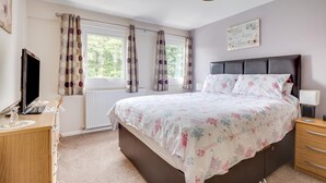 Ein Schlafzimmer mit Bett, Schreibtisch, Stuhl, Lampe und einem Fenster mit Vorhängen.