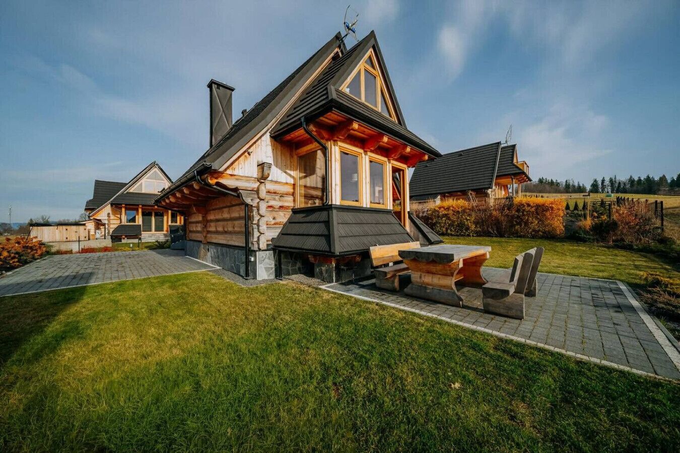 Une cabane en rondins avec un toit en pente, une cheminée et un espace patio doté de bancs.
