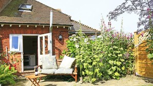 A brick house with a tiled roof, a wooden fence, and a garden with a bench and potted plants. - 1 Bed in Woodbridge (oc-hok) (Bawdsey)