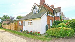 A two-story house with a white exterior, a brick chimney, and a garden with flowers and shrubs. - 1 Bed in Woodbridge (oc-hok) (Bawdsey)