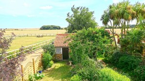 A small house with a tiled roof, surrounded by lush greenery and a fenced yard. - 1 Bed in Woodbridge (oc-hok) (Bawdsey)