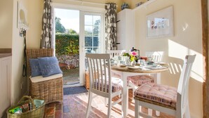 A cozy dining area with a wicker bench, white chairs, and a table set for tea. - 2 Bed in Peasmarsh (oc-rh1172) (Peasmarsh)