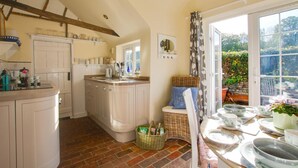 A kitchen with a central island, a dining area with a wicker chair, and a view of greenery outside. - 2 Bed in Peasmarsh (oc-rh1172) (Peasmarsh)