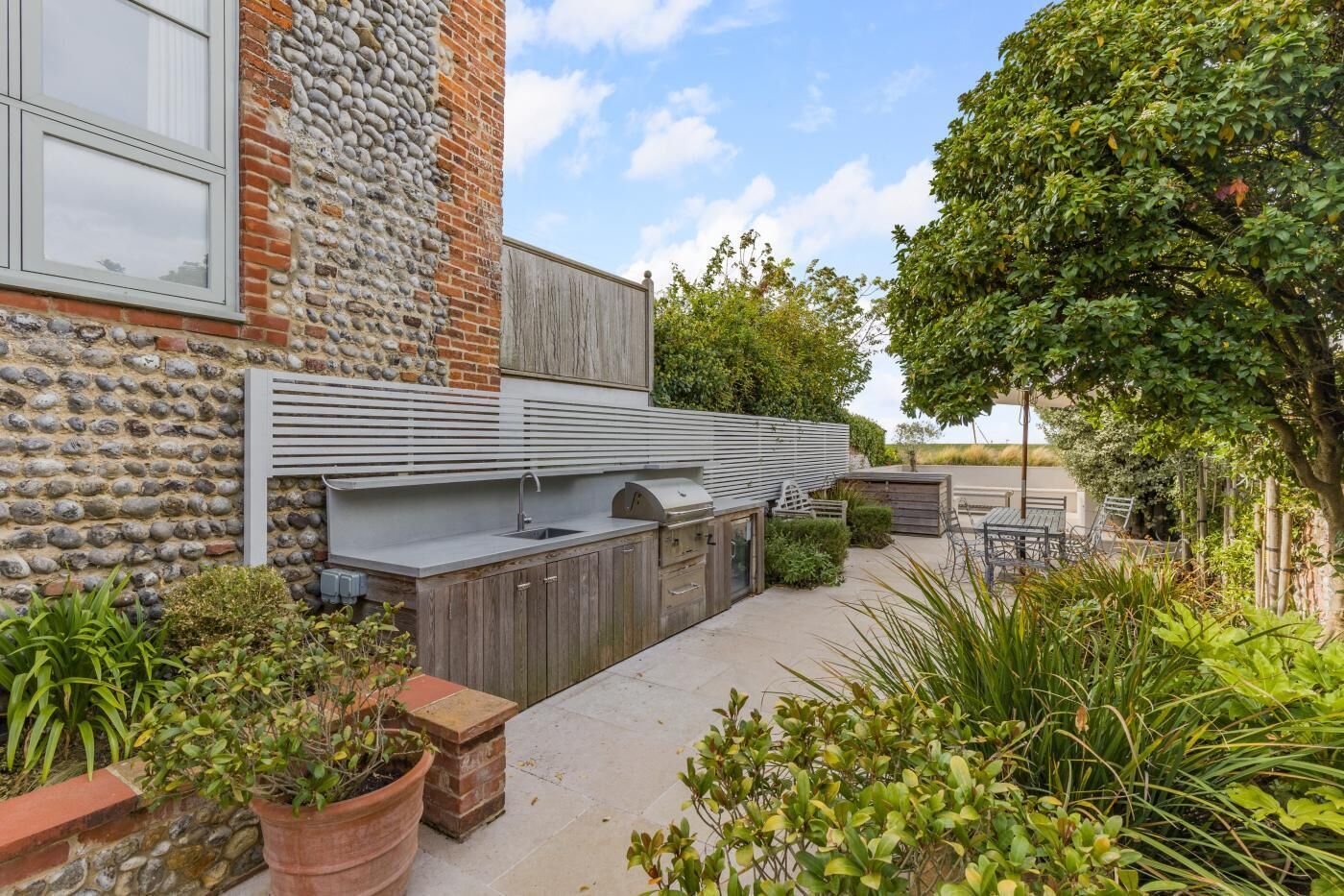 Una cocina exterior moderna con una pared de piedra, una terraza de madera y diversas plantas.