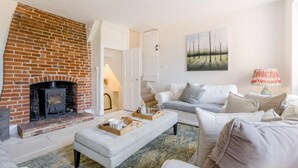Una sala de estar con chimenea de ladrillo, un sofá blanco, un tapete estampado y un cuadro en la pared.