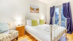 Een slaapkamer met een bed, nachtkastjes, gordijnen voor het raam en uitzicht op de omgeving.