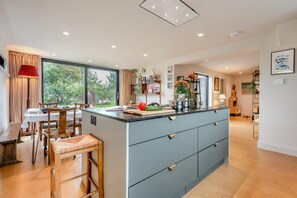 A modern kitchen with a central island, dining area with a table and chairs, and a view of the outdoors through large windows. - 3 Bed in Milford On Sea (oc-f33344) (Milford on Sea)