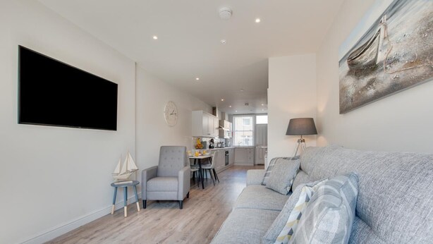 Ein modernes Wohnzimmer mit einem grauen Sofa, einem kleinen Sessel und einem Essbereich im Hintergrund.