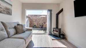 Ein modernes Wohnzimmer mit einem grauen Sofa, einem Holztisch und einem schwarzen Kaminofen.