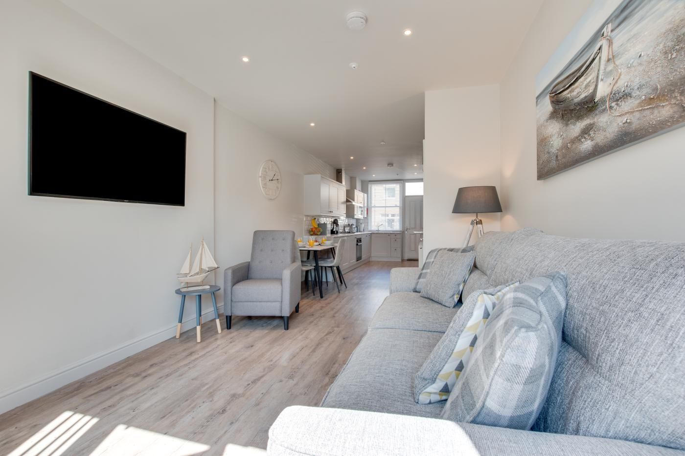 A modern living room with a grey sofa, a small armchair, and a dining area in the background.