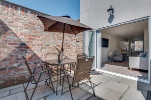 A patio with a table and chairs, a brick wall, and a glass door leading to an interior space.