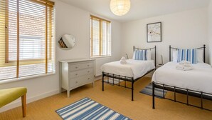 A bedroom with two beds, a dresser, a radiator, and a hanging light fixture. - 3 Bed in Southwold (oc-ftw) (Southwold)