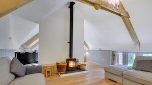 Une chambre à coucher confortable, aménagée en mezzanine, avec un plafond en bois, une cheminée intégrée, une télévision et une grande fenêtre.
