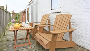 A wooden deck with two Adirondack chairs and a table with a yellow pot and white cups. - 1 Bed in Aldeburgh (oc-al105) (Aldeburgh)