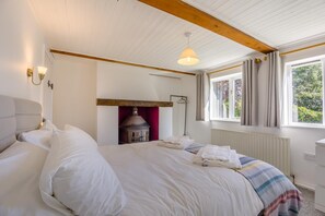 Een slaapkamer met een groot bed, een wandheater, een raam met gordijnen en een hanglamp.