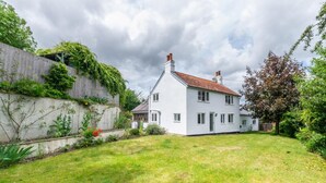 A two-story white house with a red-tiled roof, surrounded by a well-maintained garden and a wooden fence. - 4 Bed in Eastbridge (oc-bricot) (East Bridge)
