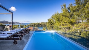 An infinity pool with lounge chairs and a view of a lake and mountains. - Villa Bella with heated pool (Barotul)