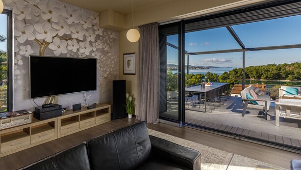 A modern living room with a large flat-screen TV, wooden entertainment unit, and a view of a pool and outdoor seating area. - Villa Bella with heated pool (Barotul)