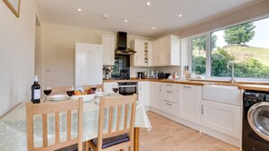 A modern kitchen with white cabinets, a dining table set with chairs, a washing machine, and a large window with a view of greenery.