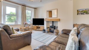 A living room with leather sofas, a flat-screen TV, a fireplace, and large windows.
