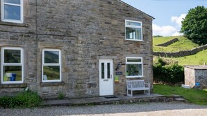 A stone building with a white door, two windows, and a bench outside.