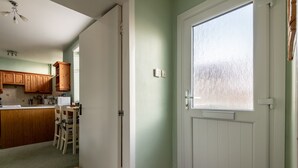 Una cocina con armarios de madera, un comedor con sillas y una puerta con ventana.